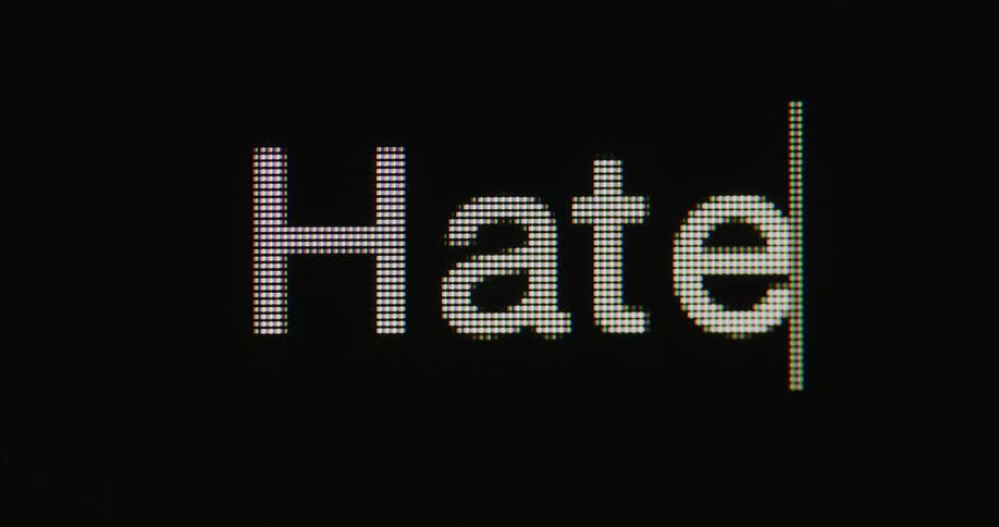 Close up of the word hate being typed in a pixelated white font followed by a blinking cursor on a black screen