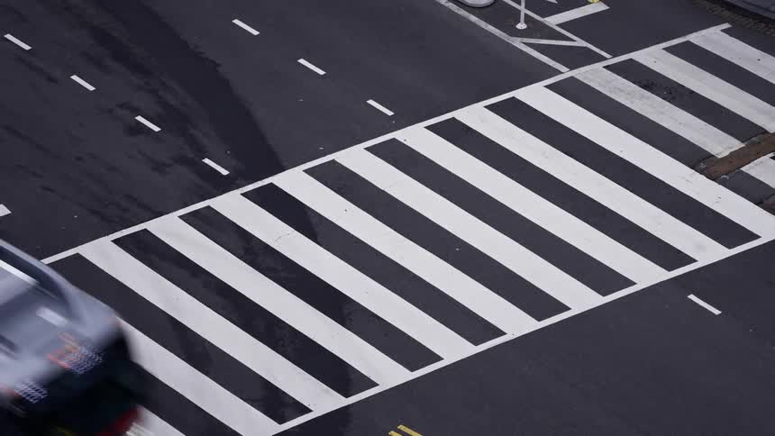 A timelapse captures a crosswalk with zebra stripes on a road showing vehicles passing by and pedestrians crossing