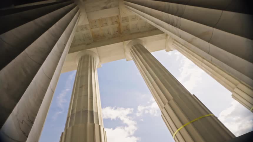 Tall marble columns support a colonnade on the outside edge of a building on a cloudy day