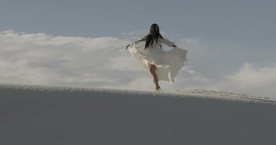 Woman in white dress dancing around in the sand