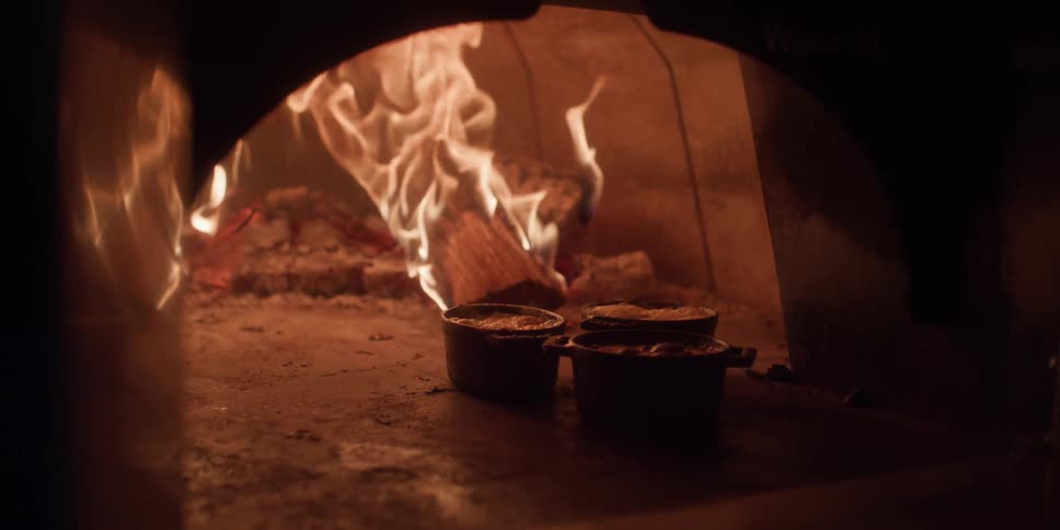 A fire burns in a large cooking oven while pots of liquid bubble away