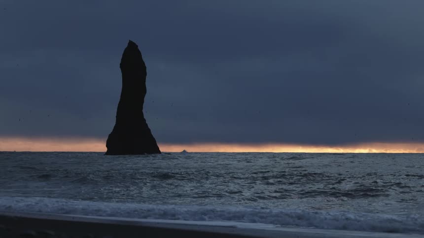 Small waves crash on a beach near a large rock