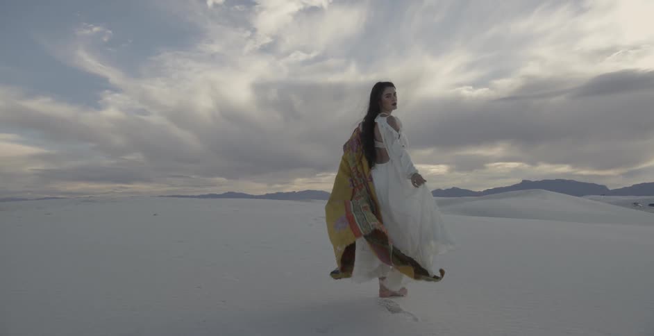 Woman in white dress walking in the sand on windy evening