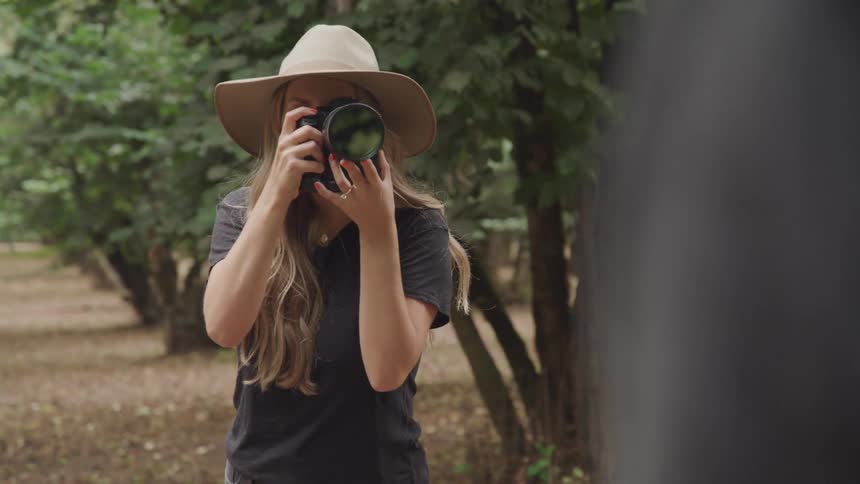 A female photographer wearing a hat is taking someones photo using a professional camera