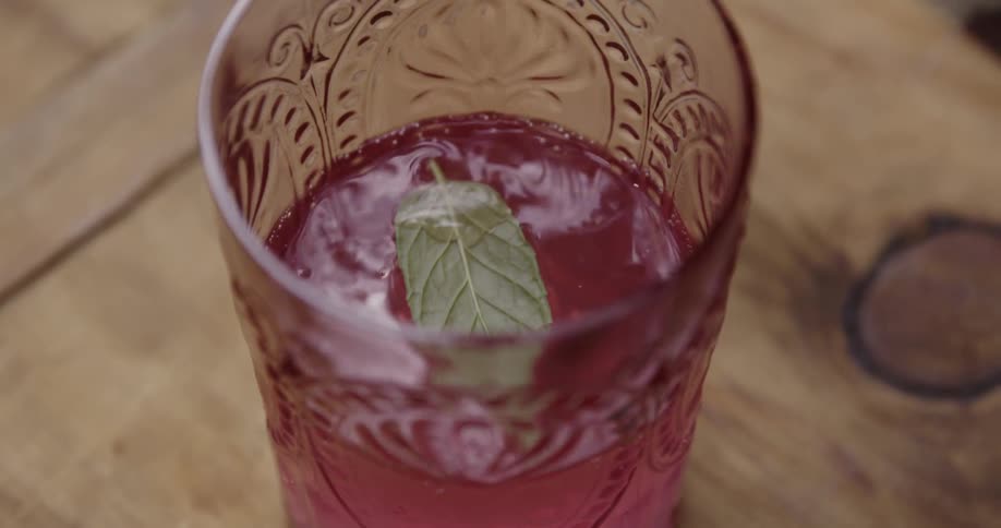 Leaf dropping into a glass of pink colored beverage