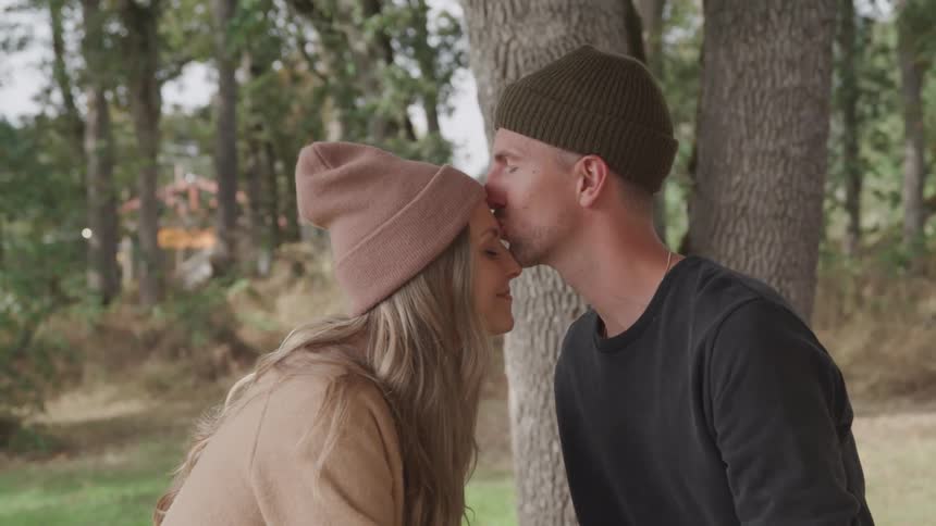 A couple kisses while standing on a forest