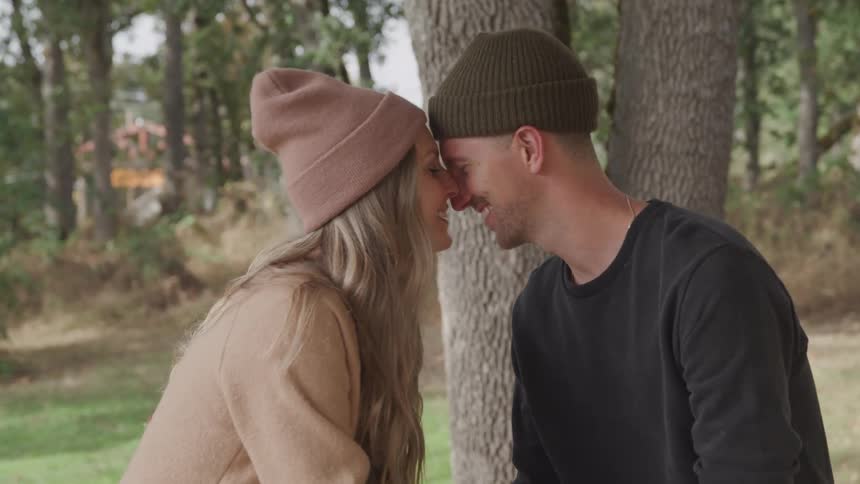 Couple in a treelined setting leaning their heads against each other in a romantic way
