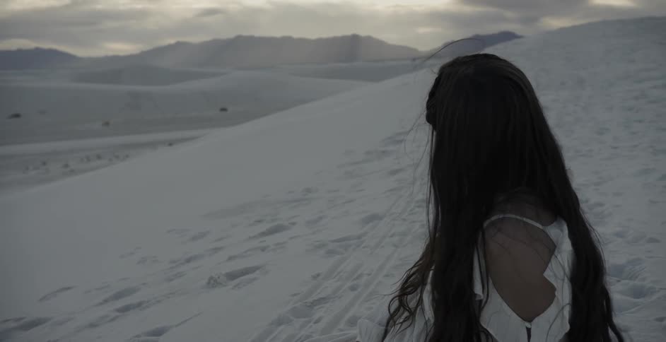 Woman in white dress standing in sand after sunset