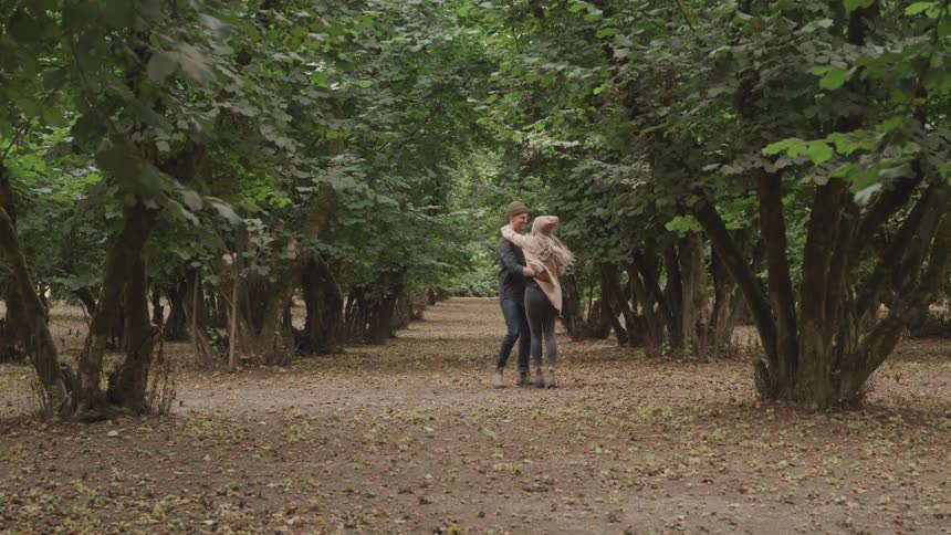 Couple holding hands running through a forest and hugging and kissing romantically