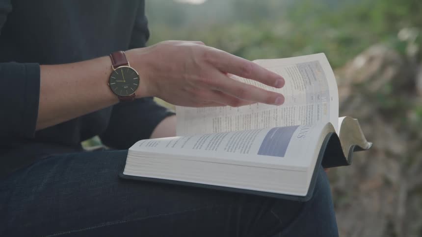 Hands of a person turning the page of a book while sitting in an outdoor setting