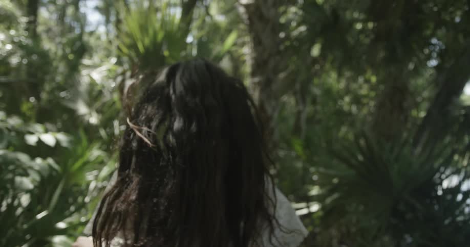 A woman's long hair flows behind her as she runs in a palm grove