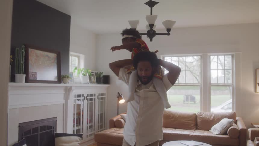 A man is with a little girl on his shoulders he is spinning in a living room and they are happy