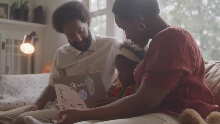 Father and mother sitting with their daughter on the sofa in the living room reading a book