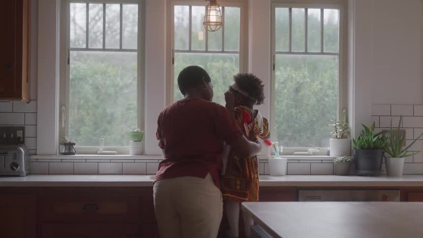 A woman holding her daughter in her arms who is in a kitchen looking out the window