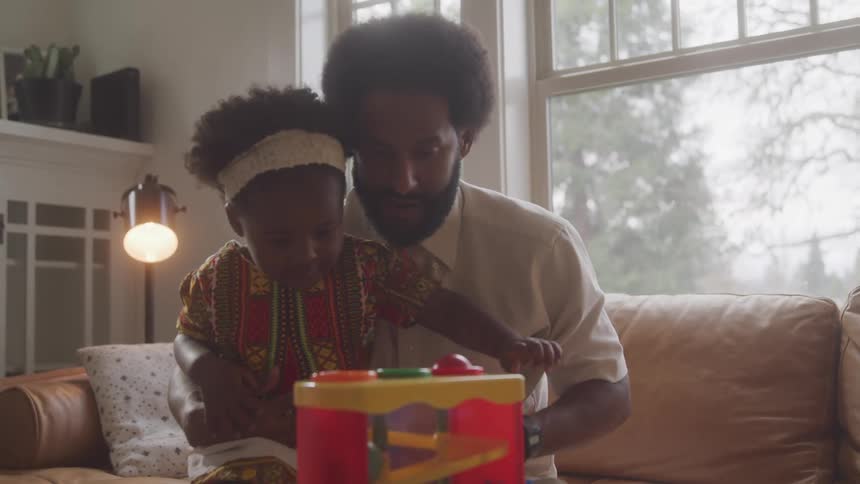 A father and daughter play with a brightly colored plastic toy in a living room