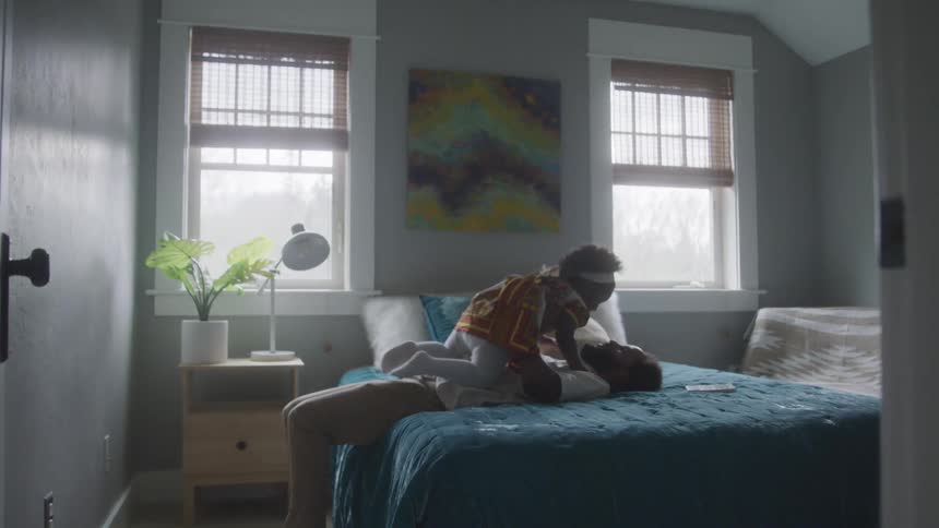 Father lying in bed holding his little daughter in his arms and playing