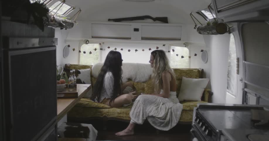 Two women sitting on a couch inside travel trailer are talking