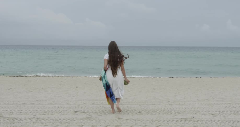 A woman is walking toward the waves on a beach during the day