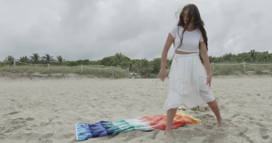 A woman is spreading out a beach towel onto the sand before she sits down