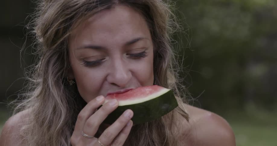 A woman is taking a bit out of a piece of watermelon and smiling