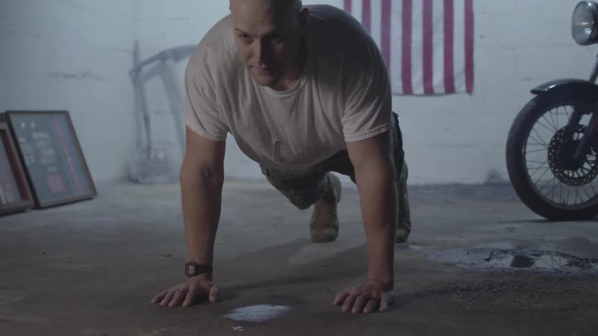 A bald man is doing pushups on a concrete floor and he is sweating