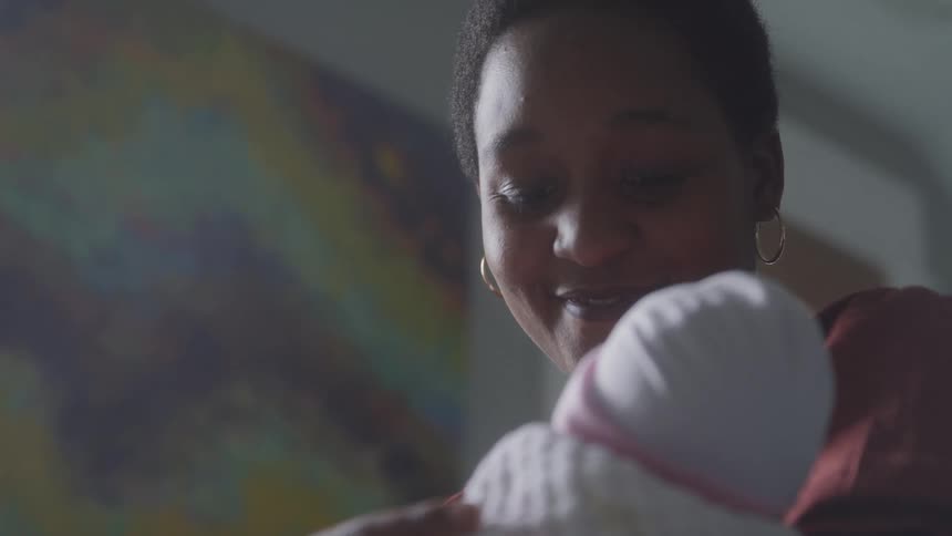 The face of a woman who is smiling while holding a newborn baby wrapped in a white blanket