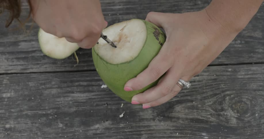 A woman uses a knife to pierce the flesh of a coconut