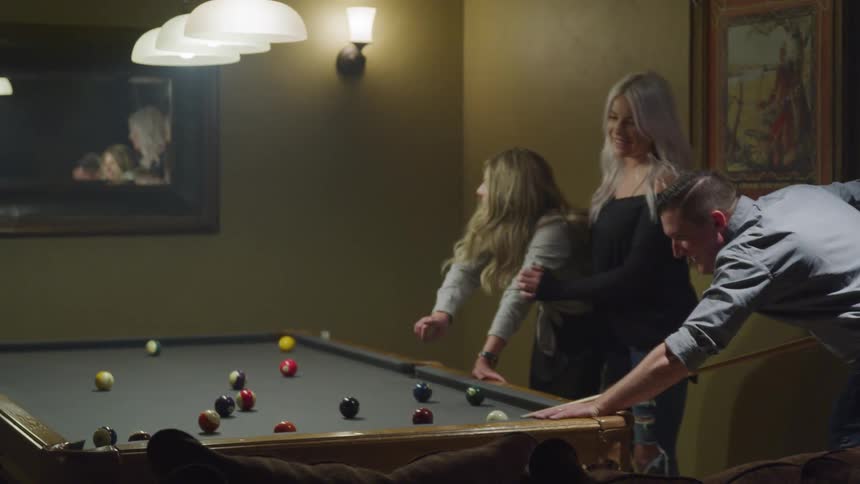 Man and two women in a room playing pool