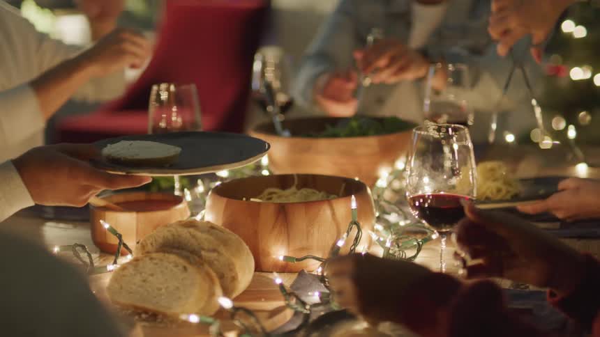 Group of people serving themselves at a dinner table with pasta breads and glasses of wine