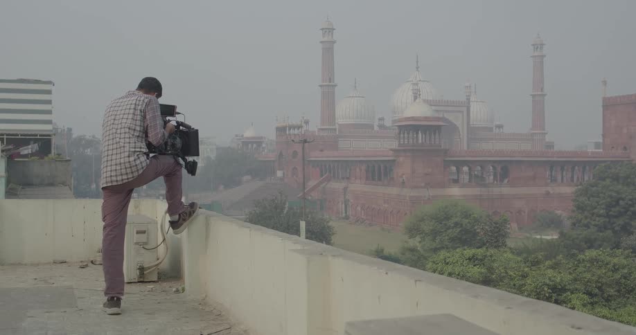 Filmmaker holding a professional video camera while standing in an outdoor terrace setting