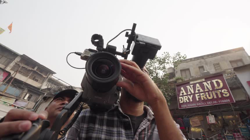A cameraman filming amidst a bustling street scene with traditional architecture and signage
