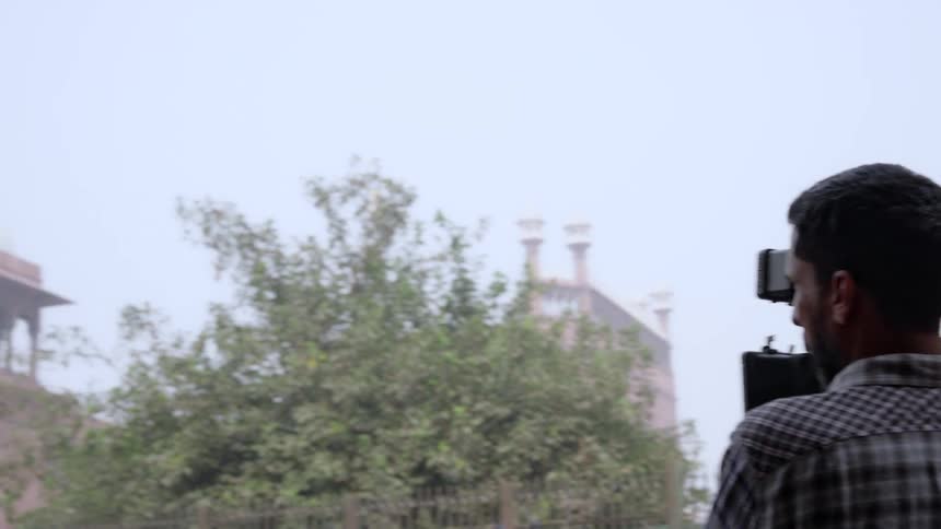 A film crew films a historic building adorned with domes and minarets in the background