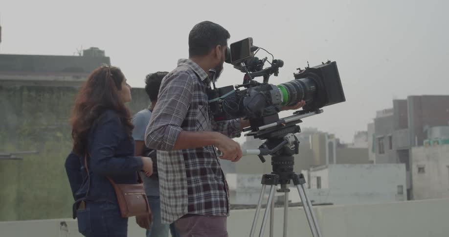 Filmmaker accompanied by two other people in an outdoor setting with buildings in the background