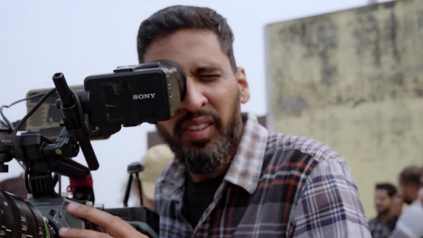 A close up of a camera lens with a mans hand adjusting the focus ring