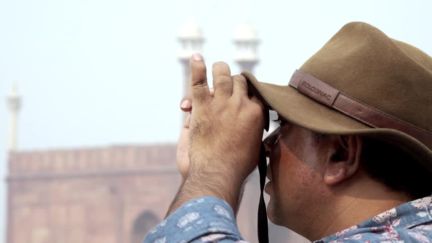 Close up of a filmmaker in a brown hat looking through a lens preparing to film