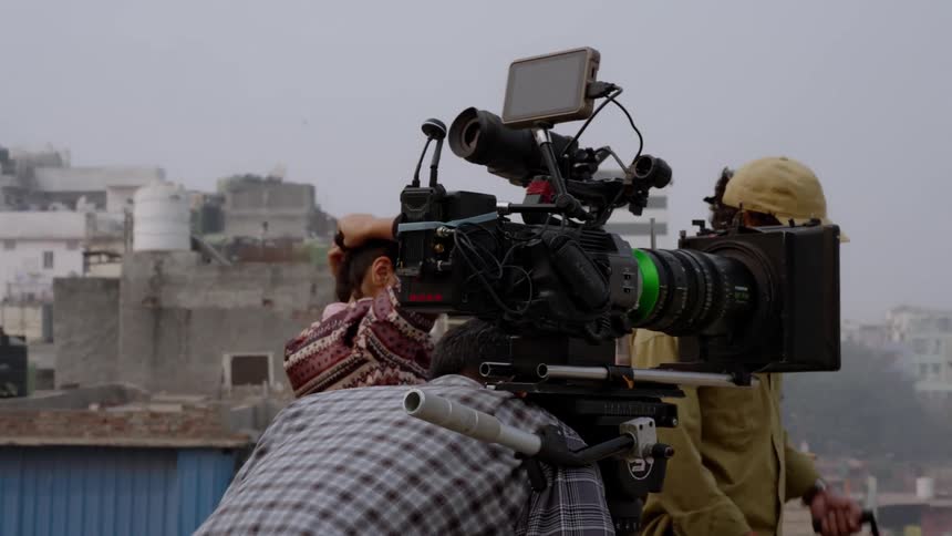 Man positioning a filming camera with crew members around