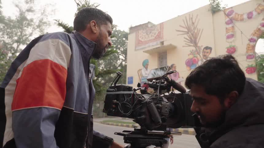 A film crew sets up a camera in front of a large mural preparing to film