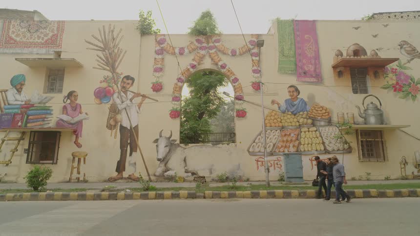 A long wall in the lodhi art district displays a vibrant mural depicting scenes of daily life