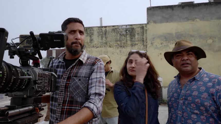 A man uses a video camera as other people stand around and talk