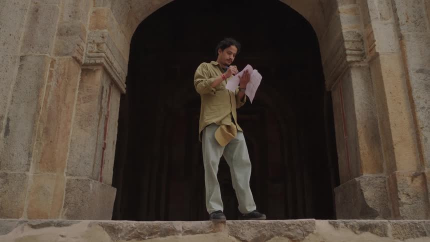 A person standing on the entrance of an old reddish brown stone structure taking notes