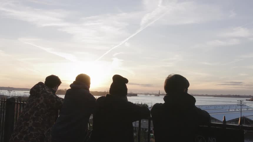 Four friends leaning on a fence looking out over a lake