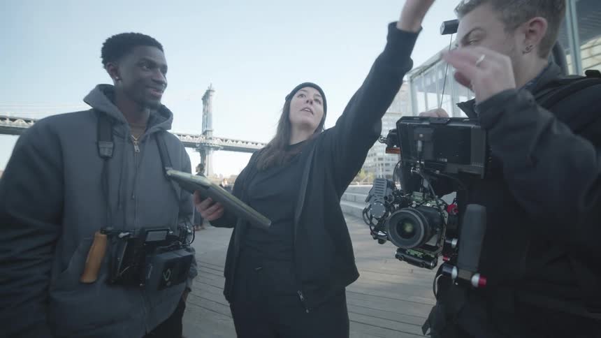 A film crew standing on a pier with cameras and equipment actively engaging in a discussion