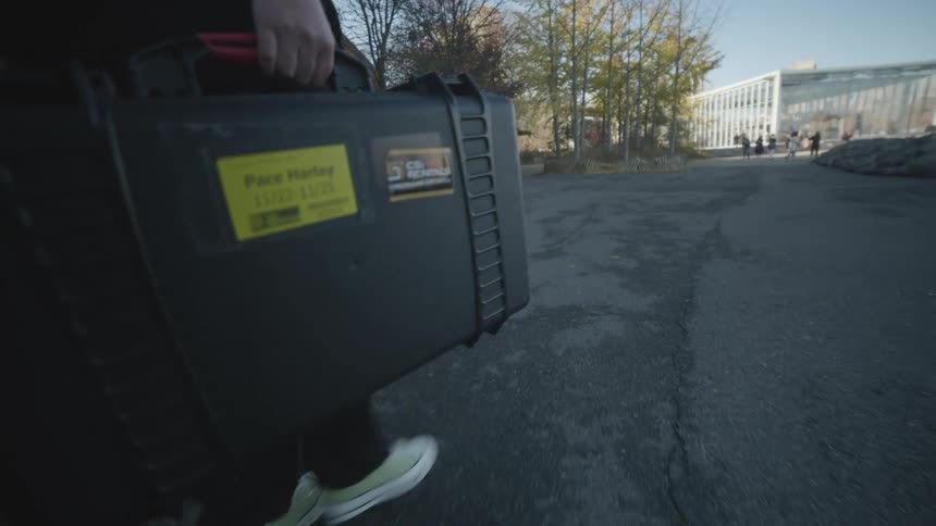 A close up of a person carrying a large black plastic case on a street