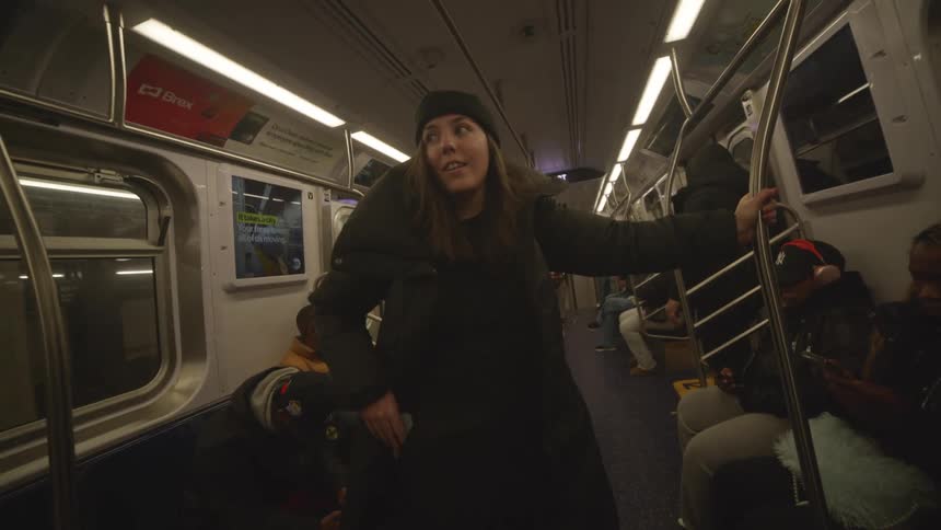 A woman in winter clothes rides the subway taking a phone out of her coat pocket