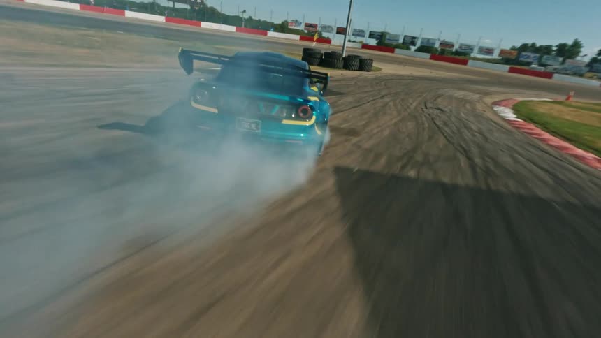 A blue and yellow race car drifts around a paved track with red and white barriers under a clear sky