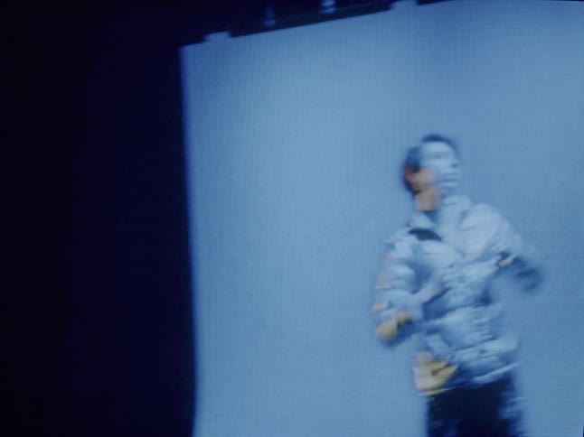 A model wearing a silver jacket poses for the camera under blue lights