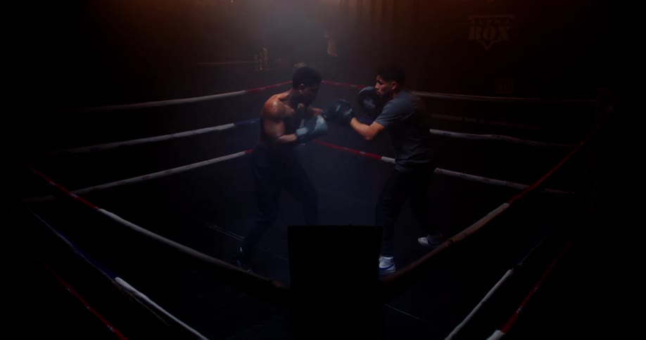 Two men boxing in a ring with low lighting