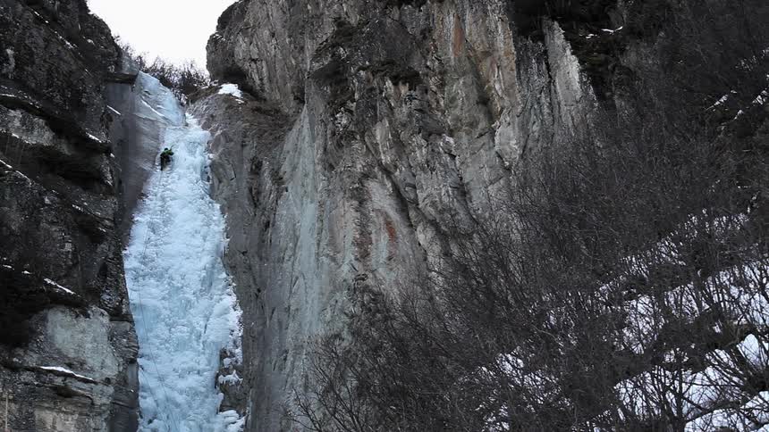A man is climbing a frozen waterfall during the day