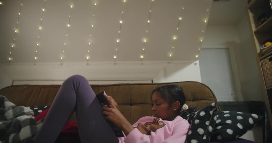 A girl resting on a couch reading a book under christmas lights in the living room