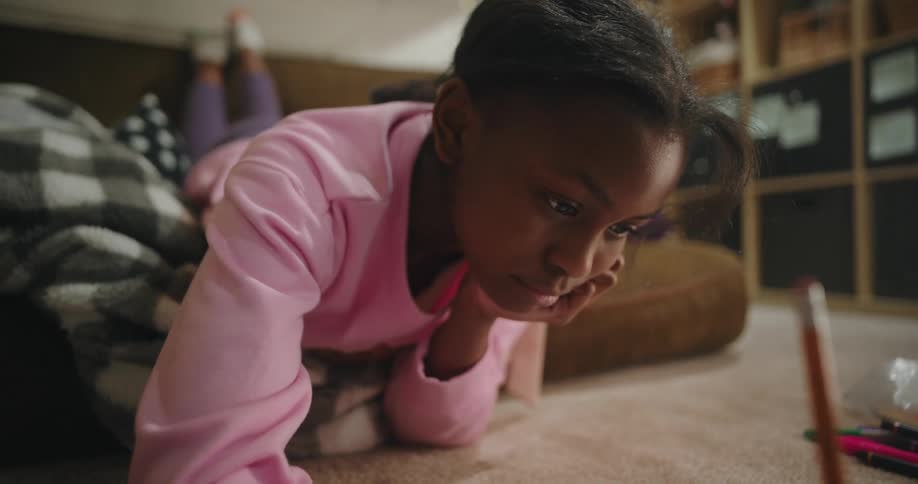 A close up of a girl laying on the living room floor writing with pencil and paper
